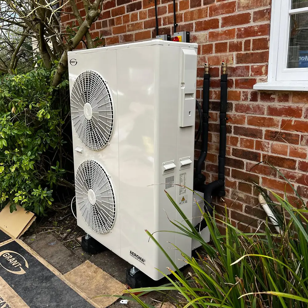 Technician servicing residential heat pump system beside Georgetown home exterior wall